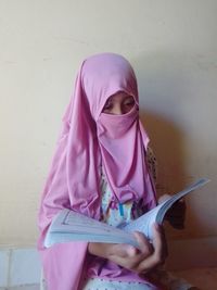 Portrait of young woman using mobile phone while standing against wall