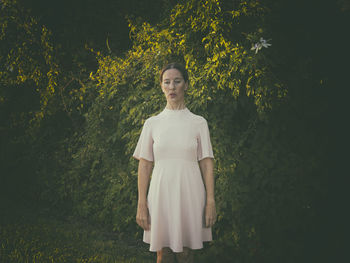 Woman in short pink dress in front of a hedge iii