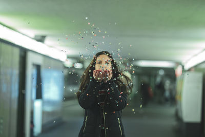 Portrait of woman blowing confetti at subway station