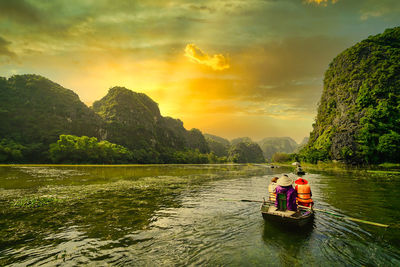 People on river against sky during sunset