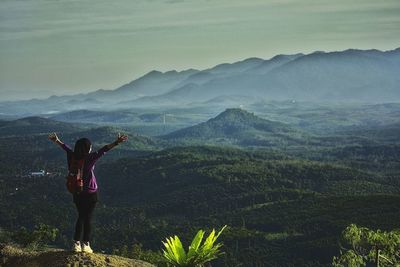 Rear view of woman standing on mountain against sky