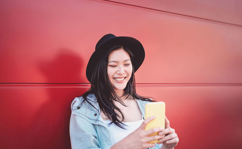 Smiling young woman using mobile phone against wall