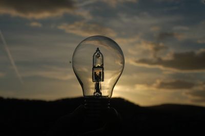 Close-up of illuminated light bulb against sky during sunset