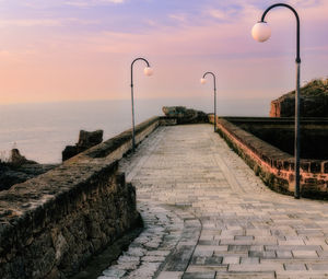 Walkway by sea against sky during sunset