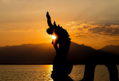 Silhouette person in sea against sky during sunset