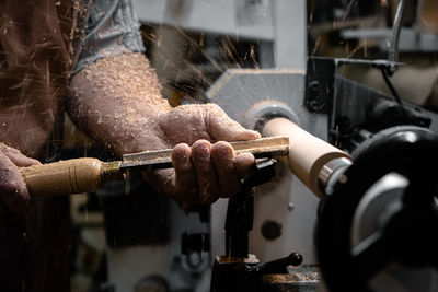 A man in a working apron works on a wood turning lathe. hands hold a chisel. hobby