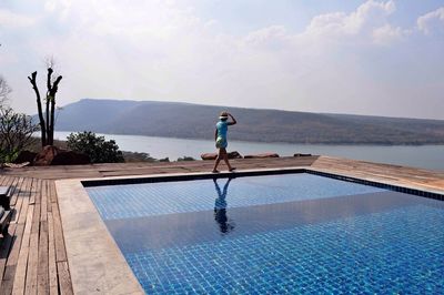 Side view of woman walking by swimming pool against mountains