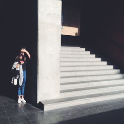 Woman shielding eyes while standing by steps on sunny day