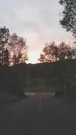 Road by trees against sky during sunset