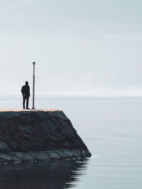 Rear view of person standing by sea against sky