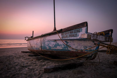 Abandoned boat moored on beach against sky during sunset