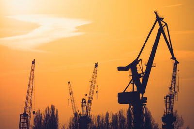 Silhouette cranes against sky during sunset