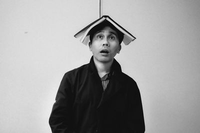 Man balancing book on head while standing by wall