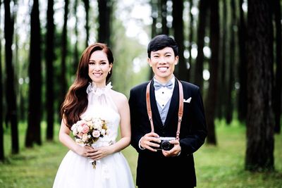 Portrait of happy wedding couple standing against trees in forest