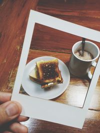 Cropped image of hand holding breakfast photograph against wooden table