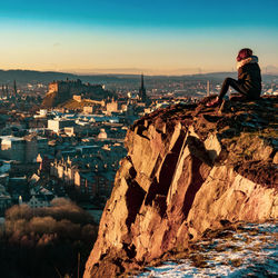 Man sitting by buildings against sky in city