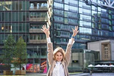 Rear view of woman with arms raised standing in city