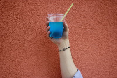 Close-up of hand holding drink against wall