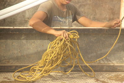 Midsection of man holding rope against wall