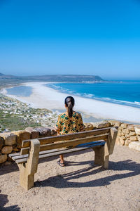 Rear view of woman sitting on retaining wall against sea