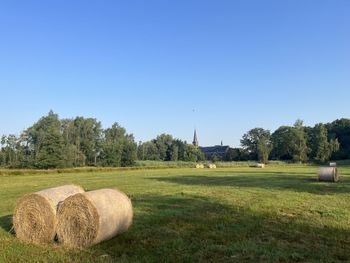 Hay bales on field against clear blue sky