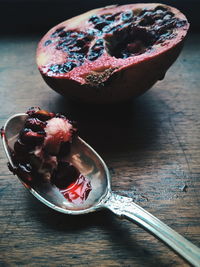 Close-up of seeds in spoon by pomegranate slice on table