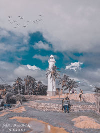 Birds flying by building against sky