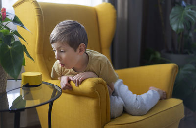 Side view of boy using mobile phone while sitting on sofa at home