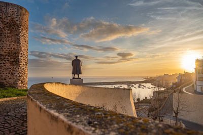 Rear view of man walking on retaining wall against sky during sunset