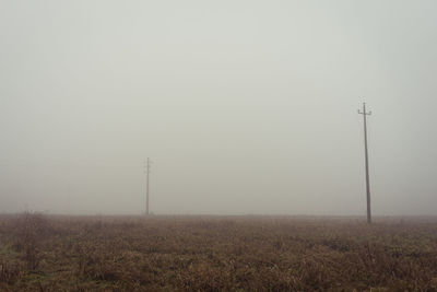 Electricity pylon on field against sky during foggy weather
