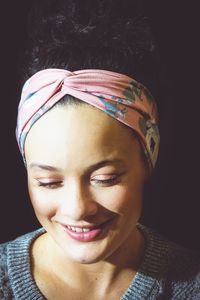 Smiling young woman wearing bandana against black background