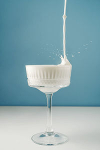 Milk pours into a beautiful crystal glass on a blue background and splashes around.