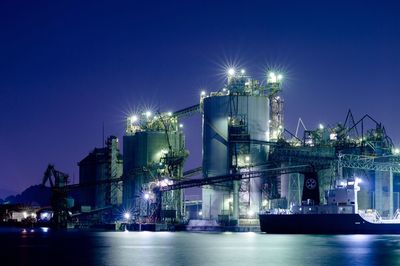 Low angle view of illuminated industry by river against sky at night