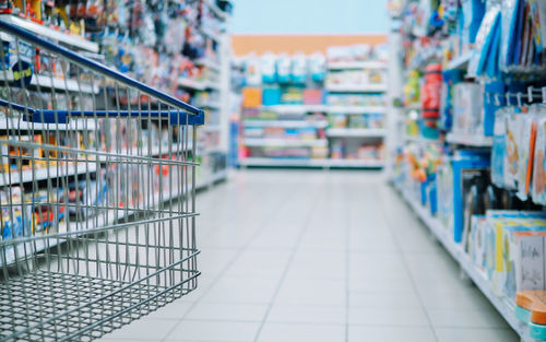 Conceptual image of shopping cart over blurry shelve of goods