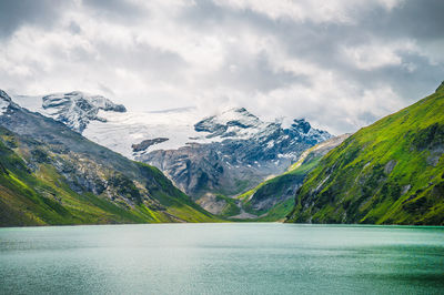 Mountains peak covered in snow and grass on a cloudy day. a big artificial lake used for hydropower.