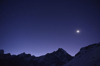 Low angle view of snow covered mountains against clear blue sky