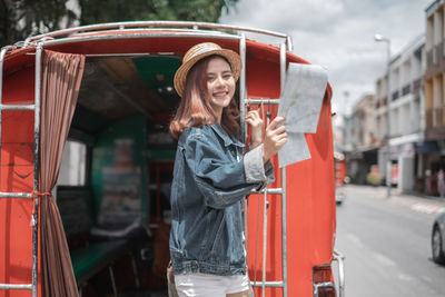 Woman holding red while standing by bus