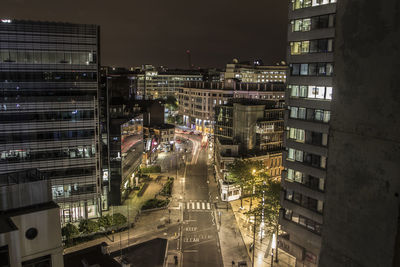 Illuminated city street amidst buildings against sky at night
