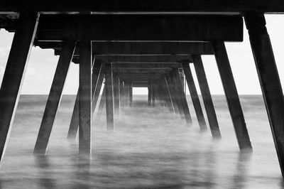 Low angle view of pier over sea against cloudy sky