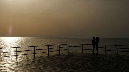 Silhouette men standing by railing against sea during sunset