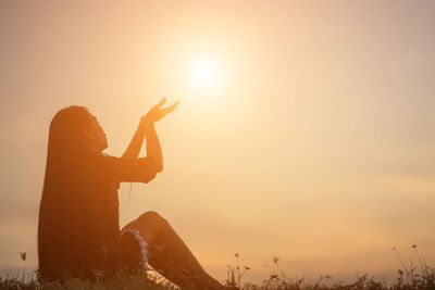 Silhouette woman sitting on land against sky during sunset