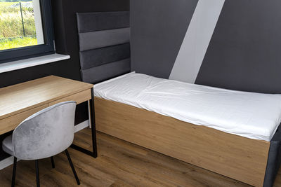 A bed and a table in a modern boy room in black and white colors, with vinyl panels on the floor.