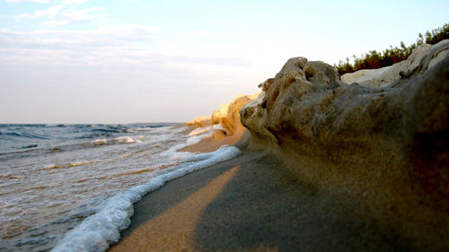 Rock formation at beach against sky during sunset