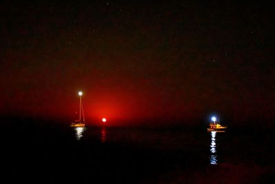 Illuminated lights on sea against sky at night