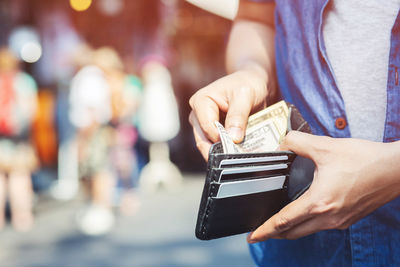 Midsection of man holding paper currency in wallet while standing on road