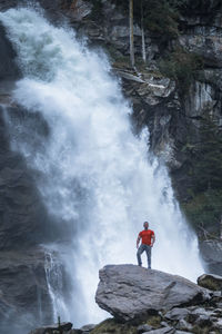 Man standing on rock against waterfall