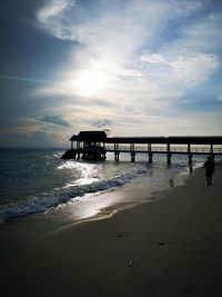 Pier on beach against sky during sunset