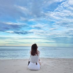 Rear view of woman sitting at beach against sky