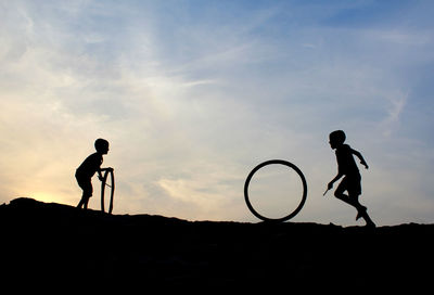 Silhouette boys playing with tires against sky