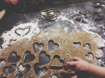 Cropped hand of child holding heart shape pastry cutter on dough